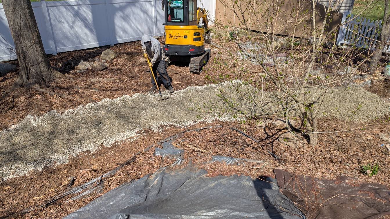 Worker grading landscape with excavator and landscape fabric installation