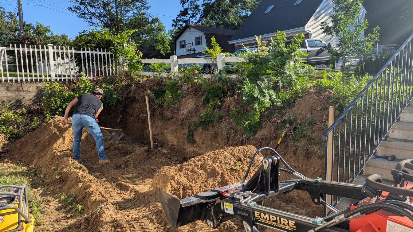 Worker performing manual excavation with Empire mini excavator in residential backyard