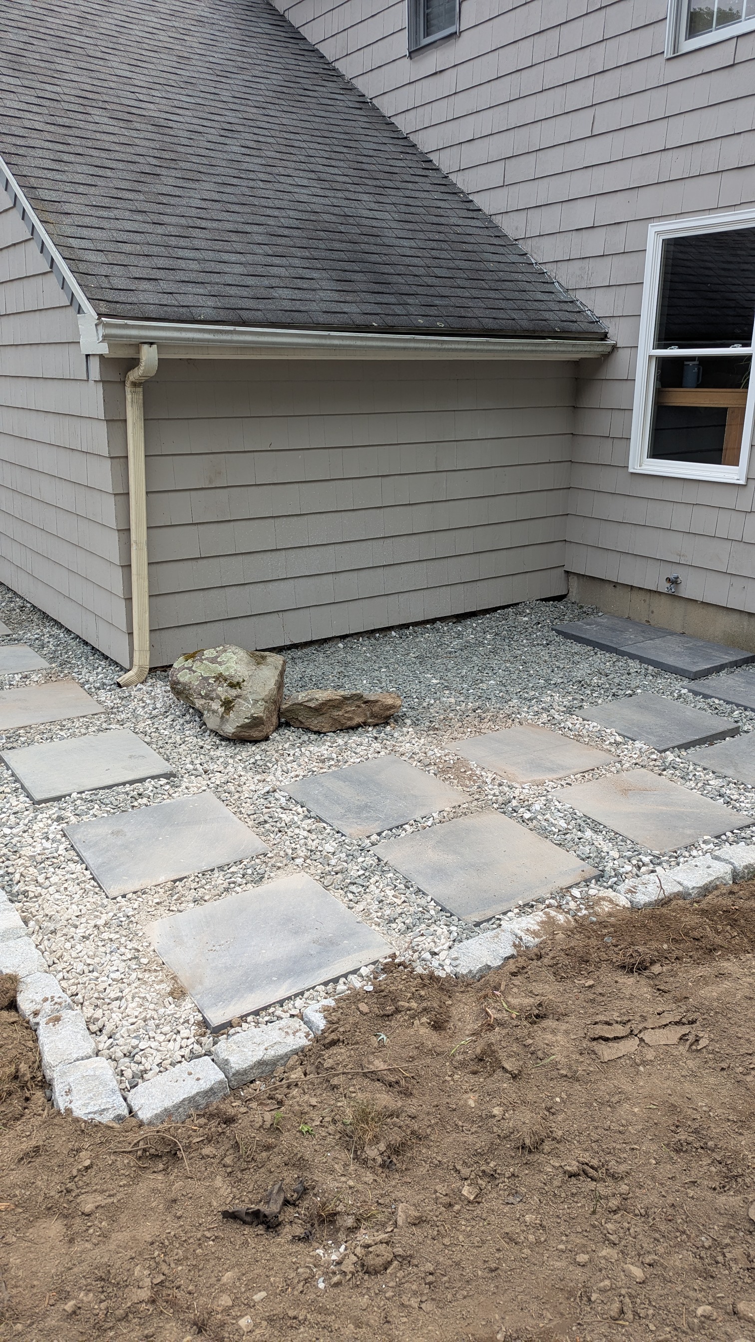Square paver patio with gravel drainage and decorative stones