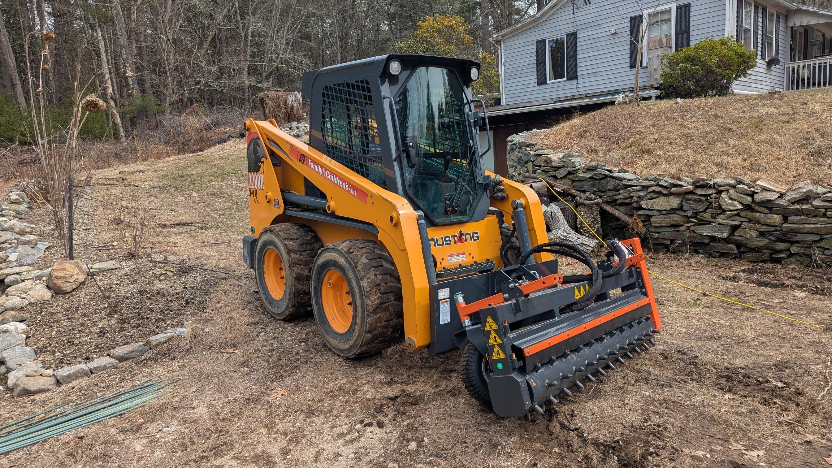 Yellow Mustang skid steer with forestry mulcher attachment for land clearing