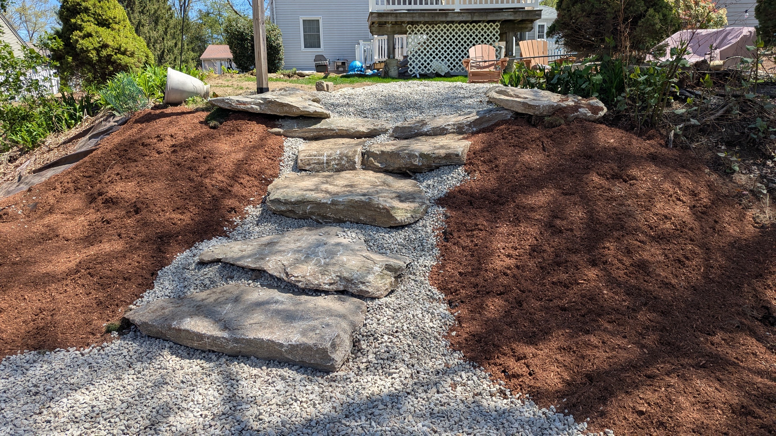 Natural stone stepping stone pathway with mulch beds leading to house